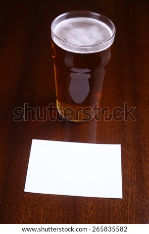 Nonic pint glass of light beer and an empty note paper on a wooden table