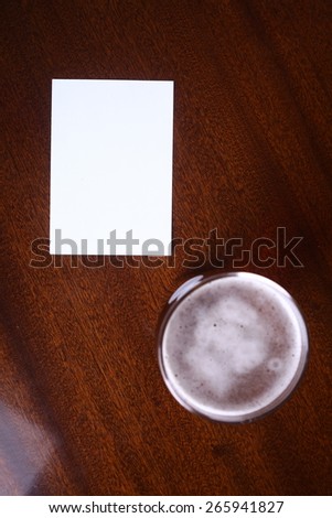 Nonic pint glass of light beer and an empty note paper on a wooden table