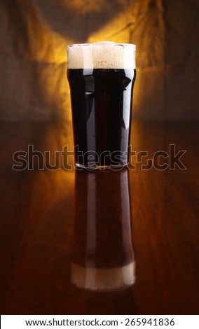 Nonic pint of dark stout beer on a table with a warm colored drapery in the background