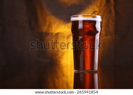 Nonic pint glass with light beer with a warm colored drapery in the background