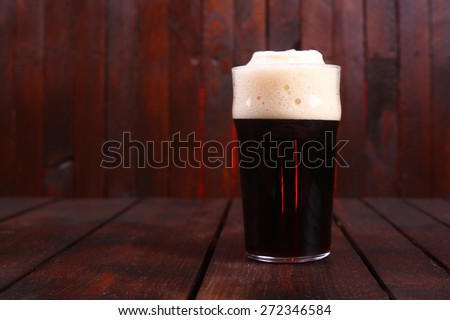 A pint glass full of dark stout ale standing on a wooden table