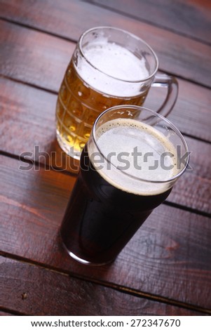 Classic mug and pint glasses full of light and dark beer standing on a wooden table