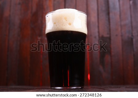 A pint glass full of dark stout ale standing on a wooden table