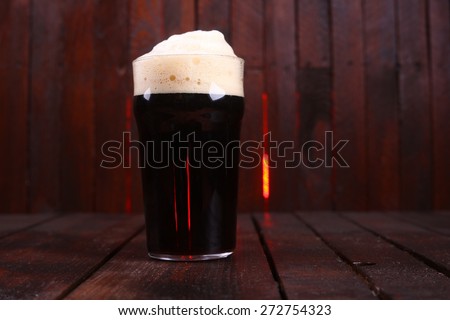 A pint glass full of dark stout ale standing on a wooden table