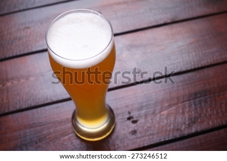 A tall glass full of light wheat beer standing on a wooden table