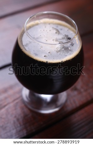 A snifter glass full of dark stout ale standing on a wooden table