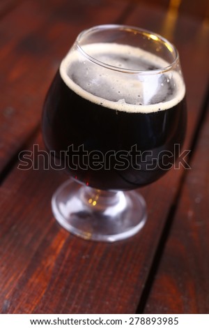 A snifter glass full of dark stout ale standing on a wooden table