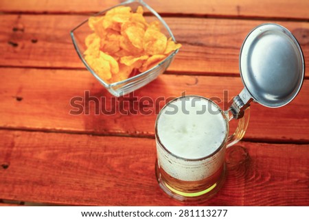 Mug full of light beer standing on wooden table with potato chips