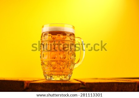 Mug full of light lager beer on a wooden table over a bright yellow background