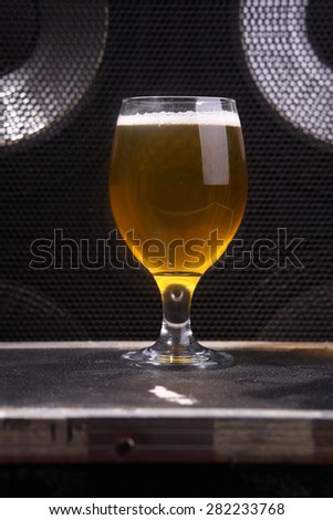 Glass full of light beer standing on a music equipment crate near a big grilled music monitor
