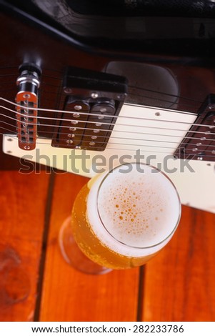 Glass full of light beer standing on a wooden table with a music equipment case and electric guitar in the background