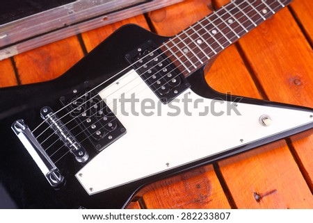 Closeup of an electric guitar body on a wooden surface with equipment case in the background