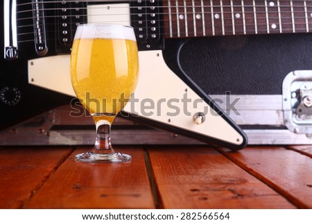 Glass full of light beer standing on a wooden table with a music equipment case and electric guitar in the background