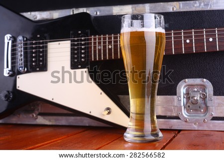 Tall glass full of light beer standing on a wooden table with a music equipment case and guitar in the background