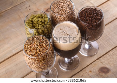 Glasses filled with dark beer, different malts and hops over a wooden background