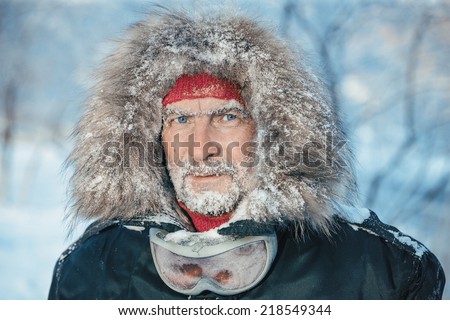 Man wearing fur with beard in snow, looking at camera