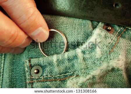 Closeup of a manÃ?Â´s hand put in or taking out a wedding ring in the worn jeans pocket. Concept of infidelity or asking in marriage.