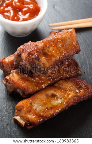 Close up of barbecue pork ribs in a slate plate with sauce and asian sticks