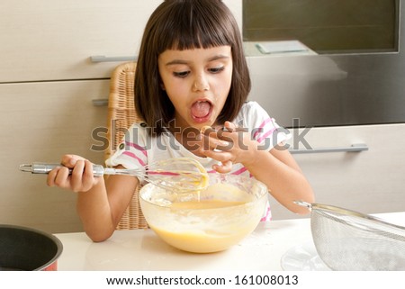 Happy little girl sucking the mixture to cook a cake