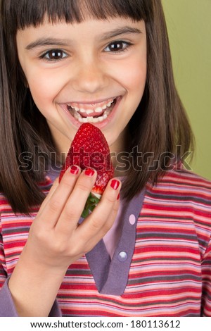 Cute and happy little girl  with red nail polish eating a big strawberry