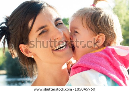 Cute baby girl biting his pretty mother laughing after bathing. Real people.