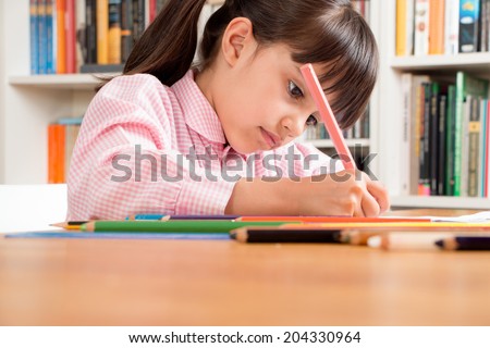 Little school girl wearing an overall doing homework