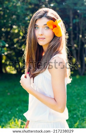 Portrait of a beautiful young woman in white dress with flower in hair outdoors