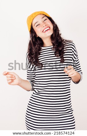 Smiling beautiful woman in striped dress and yellow wool cap dancing. Winter is coming and she is happy.