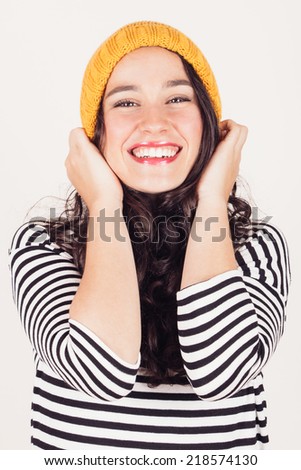 Smiling beautiful woman in striped dress putting on a yellow wool cap. Winter is coming and she is happy.