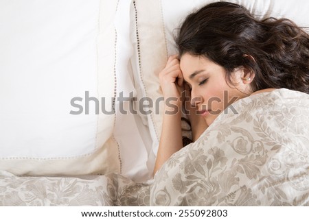 Young brunette woman sleeping in bed covered with a beige flowered quilt