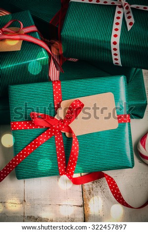 Christmas packages with green paper, red bow and brown label on a white wooden table. Lights effect added.