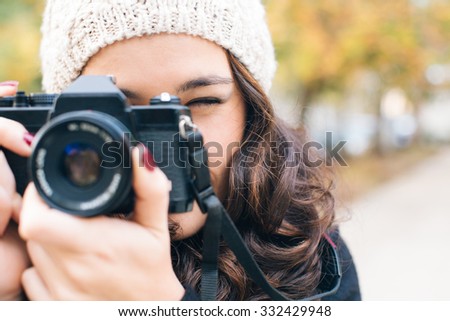 Close up of a young beautiful woman with an analog camera shooting to you in autumn