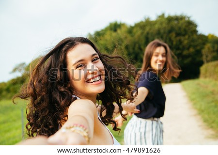 Two happy girls running in nature holding hands. Point Of View Shot.