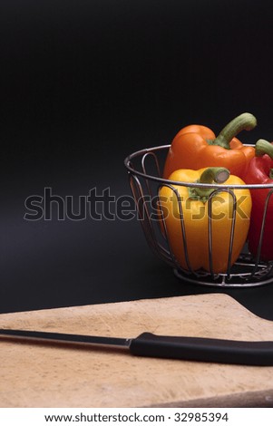 three bell peppers in chrome basket and chopping board