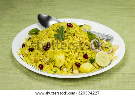 Indian breakfast Poha topped with peanuts, pomegranate seeds, chopped green chilly, lime, coriander leaves and curry leaves.