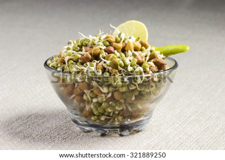 A bowl of sprout served with a green chilly and a lemon slice.