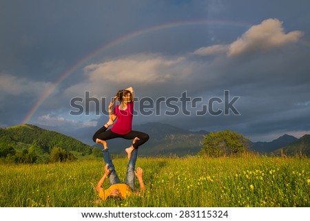 Positions Acroyoga girl of male in nature in the mountains with rainbow in the background.