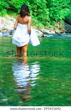 Young, beautiful and lonely bride It gets wet legs in a river.