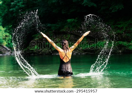 Beautiful woman in black dress playing with water in a river