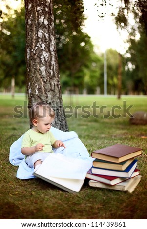 little beautiful boy reads a lot of books in summer park