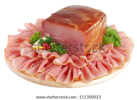 Whole cured, raw ham on round wooden board surrounded by folded slices. Isolated on white.