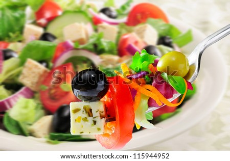 Salad with olives and feta cheese on fork with plate of salad in background.