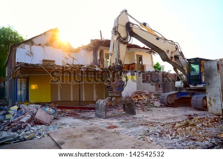 Construction/demolition site with excavator machine, partly demolished buildings and piles of rubble.