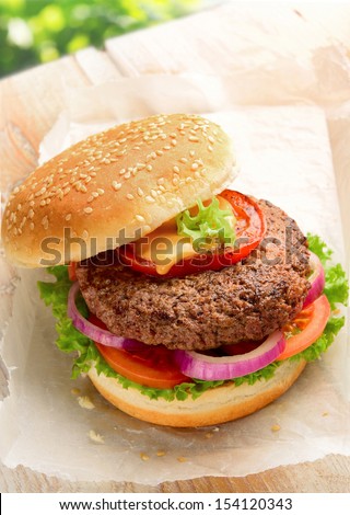 Burger Made With Pure Ground Beef. Garnished With Red Onions, Tomatoes And Lettuce On A Hamburger Bun, Topped With Sesame Seeds.