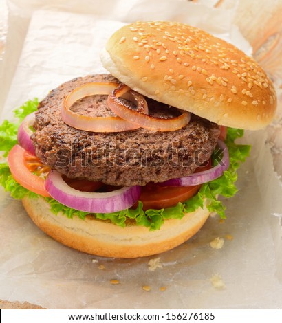 Burger made with pure ground beef. Garnished with red onions, tomatoes and lettuce on a hamburger bun, topped with sesame seeds.