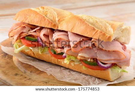 Ham and salad submarine sandwich from freshly cut baguette on rustic wooden bread board.
