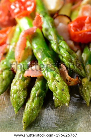 Green asparagus dish grilled in olive oil with ham, garlic and tomato. Close up with selective focus on asparagus tips.