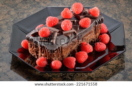 Rich chocolate fudge cake with raspberries in black octagonal dish.