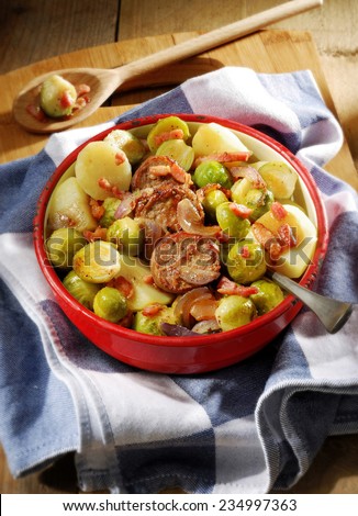 Winter meal. Seasonal fare of potatoes, Brussels sprouts and sausage slices garnished with onion and bacon in rustic enamel serving dish.