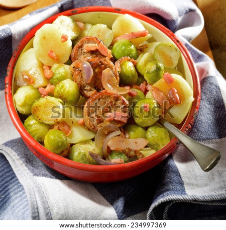 Winter meal. Seasonal fare with potatoes, Brussels sprouts and sausage slices garnished with onion and bacon in rustic enamel serving dish.